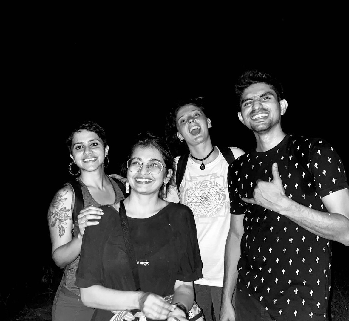 Four young Indian people - two men and two women - are standing close to each other smiling in a black and white photo taken at night.